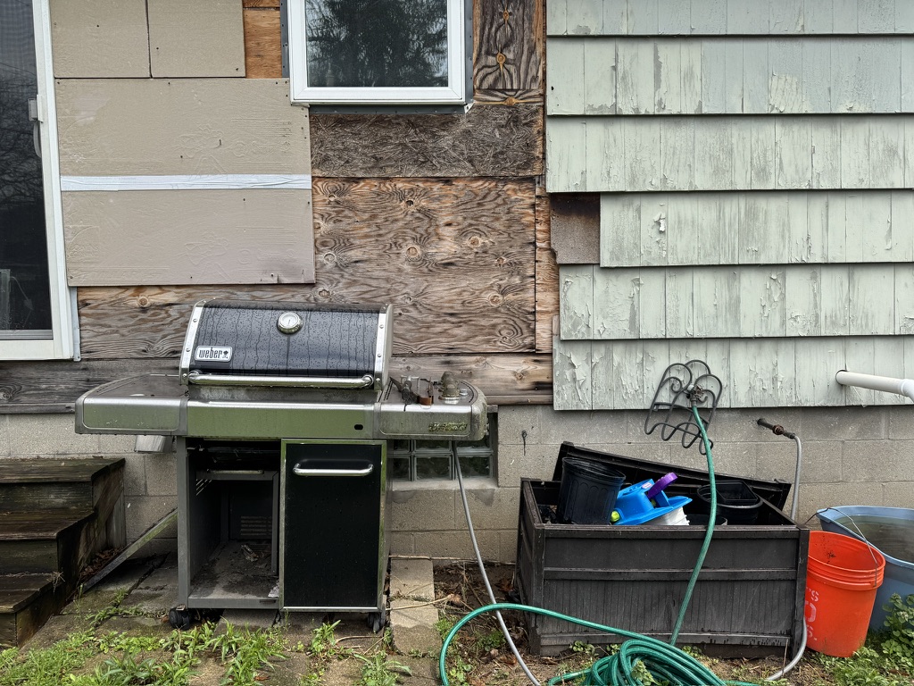 Exposed sheathing and missing siding next to grill